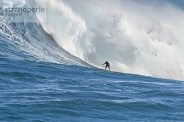 A tow-in surfer (MR) drops to the curl of Hawaii's big surf at Peahi (Jaws) off Maui  Hawaii  USA.