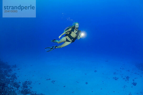 A female diver (MR) above the reef in mid water shining a light  off the island of Yap  Micronesia.