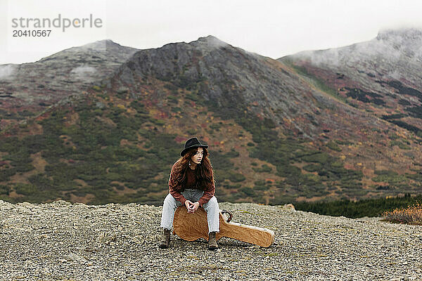 Teenage girl wearing a black hat  sitting on her guitar case in the fall at Glen Alps  in Anchorage  Alaska