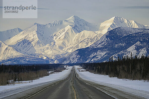 The Alaska Highway reaches into the distance as the St. Elias mountains loom in the distance. This is on the way to Haines Junction  Yukon on a glorious winter day.