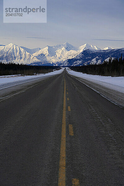 The Alaska Highway reaches into the distance as the St. Elias mountains loom in the distance. This is on the way to Haines Junction  Yukon on a glorious winter day.