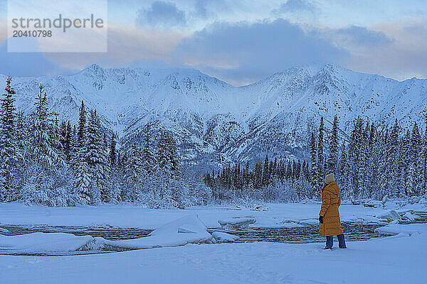 Woman standing in the snow admiring the snow covered landscape of the Wheaton River Valley as the sky gradually illumnates.