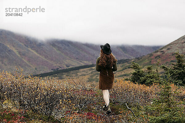 Teenage girl wearing a black hat and a brown jumper dress walking in the fall at Glen Alps  in Anchorage  Alaska