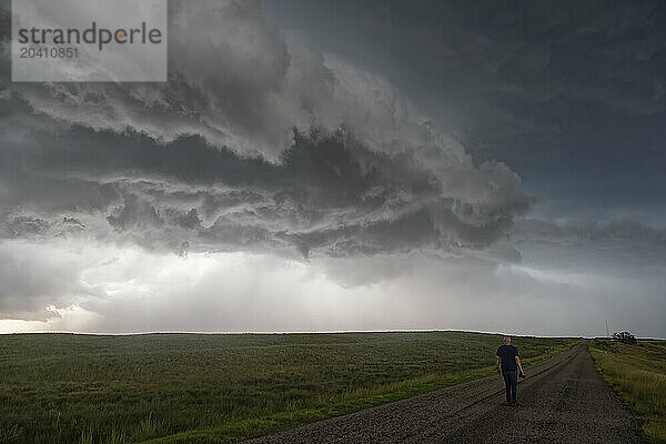 Person walking on a road while a huge thunderstorm is rolling across overhead.