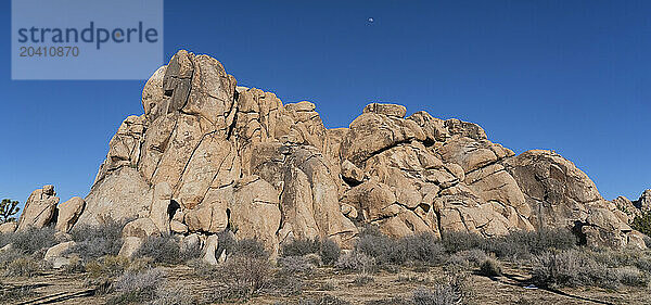 Striking rocks in Joshua Tree National Park located in southern California. The moon can be seen in the sky above the monolith.