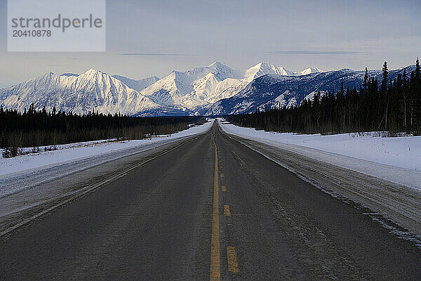 The Alaska Highway reaches into the distance as the St. Elias mountains loom in the distance. This is on the way to Haines Junction  Yukon on a glorious winter day.