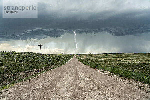 Lightning bolt strikes from a thunderstorm while a lonely road leads into the storm.