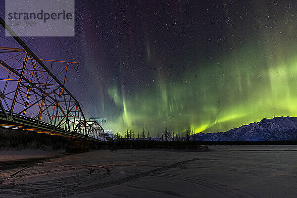 Green and purple northern lights at Old Knik Bridge in Palmer  Alaska in view of the mountains