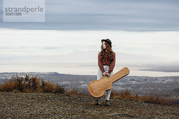 Teenage girl standing  holding her guitar case in the fall at Glen Alps  in Anchorage  Alaska