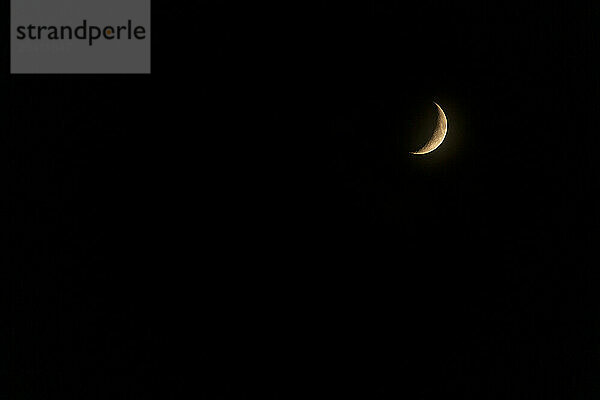 A crescent moon glowing with the warm light of the sun in a black sky