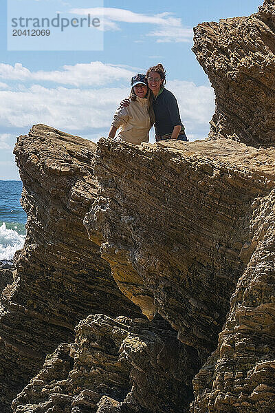 Two women hug on top of stratified rock at Crystal Cove State Park near Irvine  California.