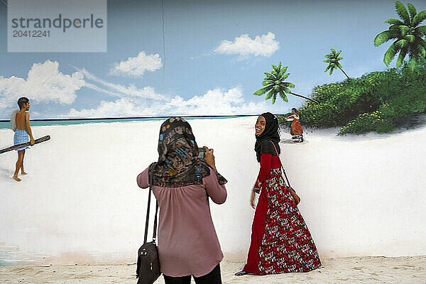 People by becoming pictures next to a painted wall on the street. Male City. Maldives