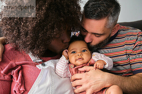 Multiracial family  parents kissing their baby girl.