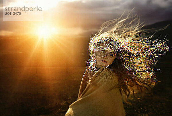 Beautiful young girl with hair blowing in bright sunny field