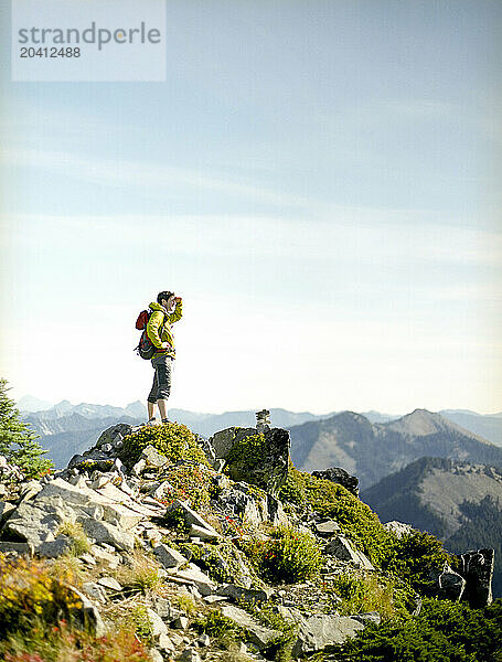 A male hiker on a mountain top looks off into the distance.