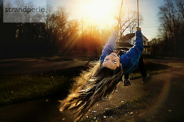 Young girl long hair playing on swing sunny yard