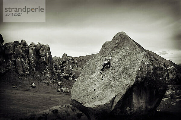 A young man rock climbs up the face of a large  limestone boulder in Castle Hill  New Zealand.