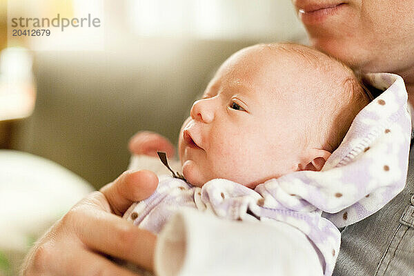 A father holds his newborn smiling baby in his arms in his living room.