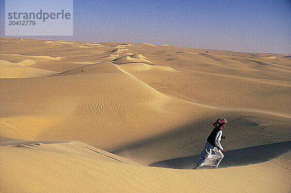 Bedouin desert guide strides across massive dune ridge. Great Sand Sea  south of Siwa Oasis. Egyptian Western Desert (natural co