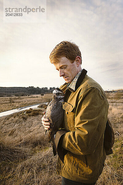 A falconer comforts and hold his goshawk close during a hunt.