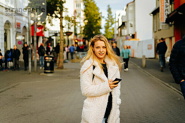 Smiling woman using mobile phone on the street.