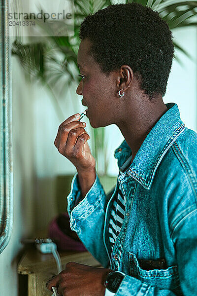 young short haired african young woman putting lipstick