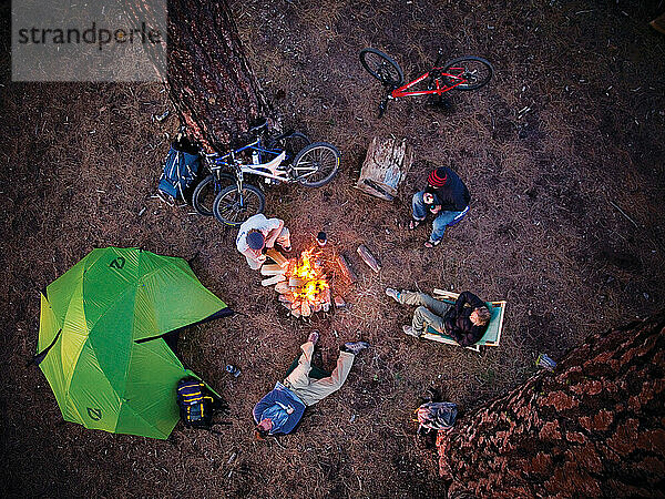 Friends gather outside their tent around the camp fire at a picnic on the beach.