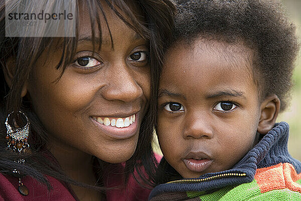 An African American mother holds her two-year-old son close to her face and smiles into the camera.