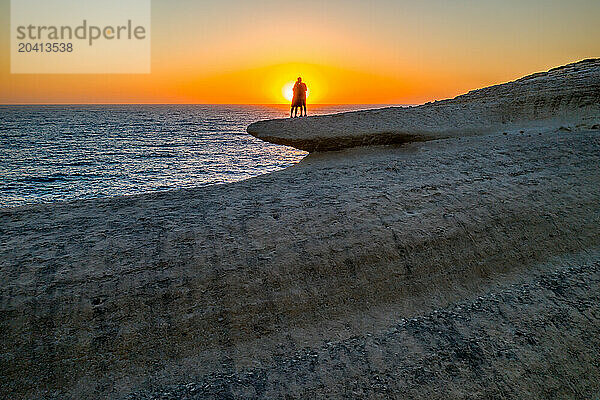 Silhouette view of couple hugging eachother on top of a sea cliff