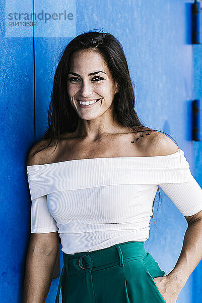 Portrait confident smiling young woman against a blue wall