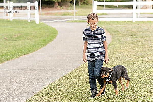 Smiling Boy walking with black rottweiler dog on the grass