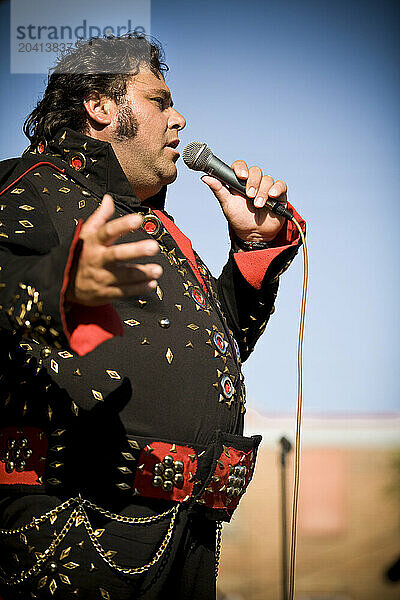 Elvis impersonator in a black costume sings for the crowd.