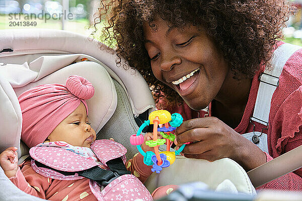 African woman is holding a toy for a baby girl in a baby stroller.