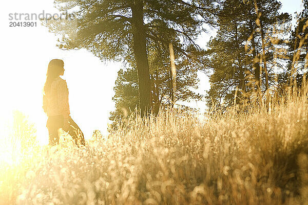 A backlit  young woman smiles and poses for a portrait in a large  grassy field near Flagstaff  Arizona.