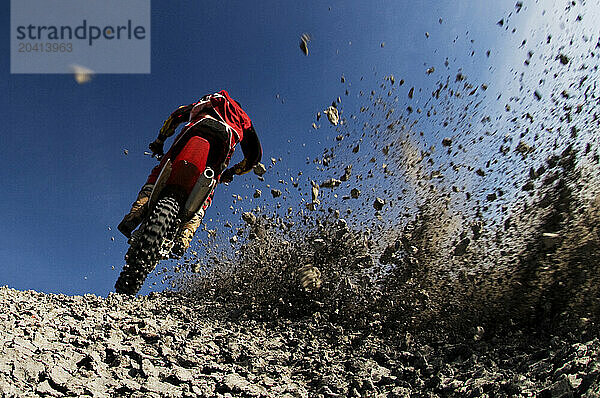 Dust and dirt fly as a young man climbs a steep hill on his dirt bike into a hard turn while motocross riding on the surreal dunes near Cameron  AZ.