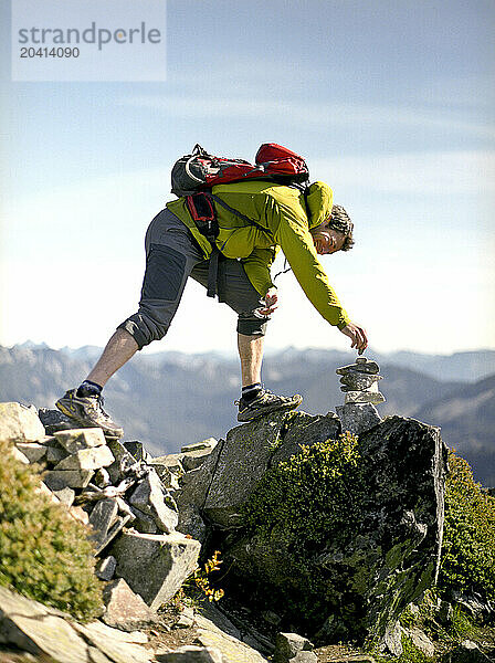 A hiker on a mountain top builds a rock cairn.