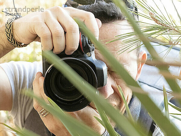 Close up of a professional photographer taking photos behind leaves