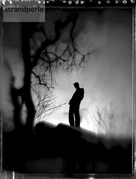 Selective focus  black & white sillouette of a figure thinking near a wintery tree