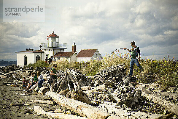 A young father carrying his baby in a sling walks with a stick over driftwood with his family.