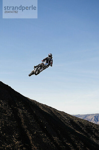 A young man jumps his dirt bike high in the air while motocross riding the surreal dunes near Cameron  AZ.