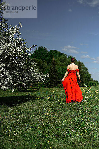 a girl in a red dress walking into the distance in nature