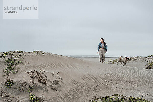 Woman Walking Dog on Sandy Dunes on cloudy day