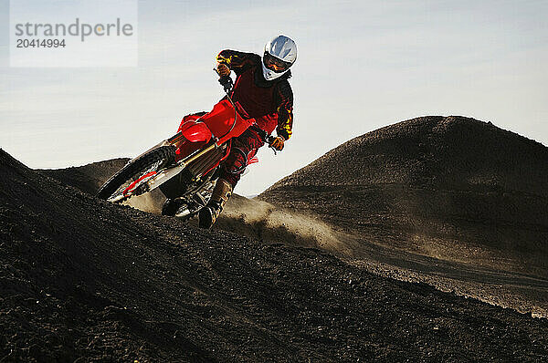 Dust and dirt fly as a young man banks his dirt bike into a hard turn while motocross riding on the surreal dunes near Cameron  AZ.