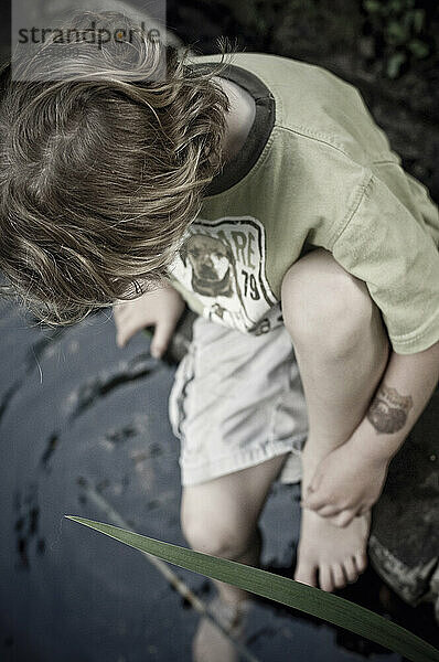 A young boy sitting by a pond.