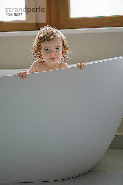 A small smiling girl is sitting in the bathroom.