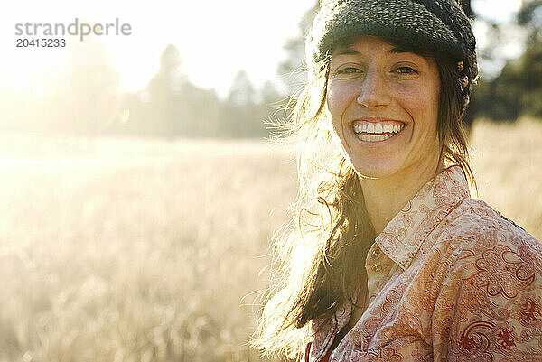 A backlit  young woman smiles and poses for a portrait in a large  grassy field near Flagstaff  Arizona.