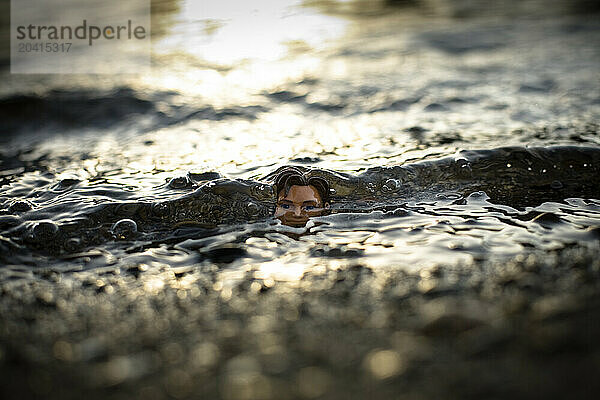 Waves roll over a half submerged male doll head  in Couer D'Alene ID.