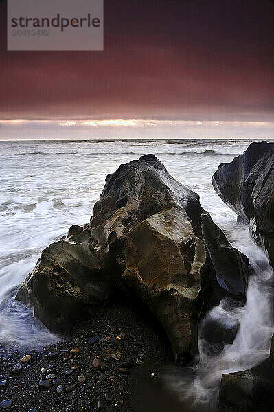 Waves crashing over a beach boulder on Ruby Beach in Olympic National Park at sunset.