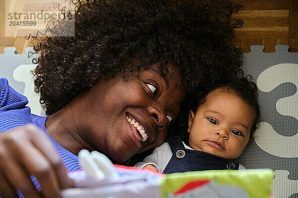 African woman is laying on the floor with a baby reading a book.