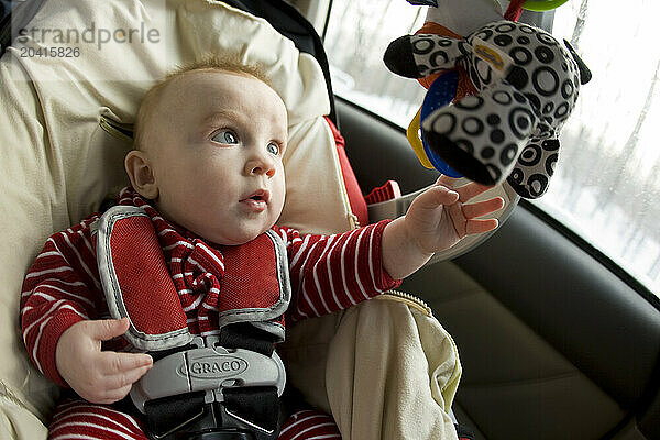 A baby in a car seat plays with a toy.